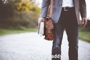 Arquetipos: El mentor Se ve la parte baja de un hombre, que sostiene un libro gordo en la mano y lleva puesto un morral. Esta vestido casualmente. Parece ser un Profesor, o talvez un Mentor. Podria ser uno de los arquetipos del Sugar Daddy.