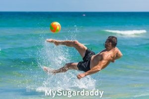 Seducir a un hombre: el niño interior En la imagen se ve a un hombre pateando una pelota saltando al mismo tiempo del agua. Se encuentra en una playa. Si queremos seducir a un hombre, hay que tocar el niño interior