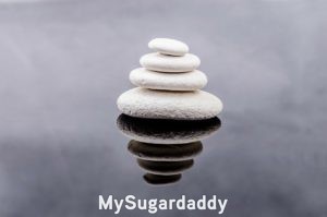 Relajar: encontrar el equilibrio La imagen muestra una torre de piedras bien equilibradas. Estan sobre un lago y el reflejo es como un espejo. Relajar significa estar en sintonia con el entorno, al igual que esta torre de piedras.