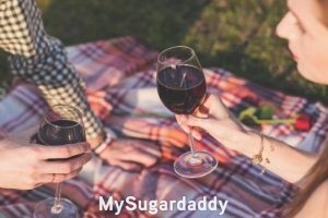 Cómo conversar con una Sugar Baby: encuentro romántico ¿Cómo conversar con una Sugar Baby?: Vemos a dos personas sobre una cobija. Están sentados sobre ella. Parece ser un picnic o algo similar. Comparten unas copas de vino y disfrutan de una conversación. El no se puede ver, pero ella sí. Se nota que es una mujer joven y atractiva.