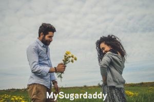Manual para ser una Sugar Baby: Cita Manual para ser una Sugar Baby: En la imagen podemos ver un momento romántico y casual. Un hombre y una mujer están parados de frente y se sonríen. Él tiene flores en la mano y se las ofrece a ella. Así nacen buenas relaciones y una Sugar Baby debe ambicionar estos momentos para tener un Sugar Daddy en su vida.